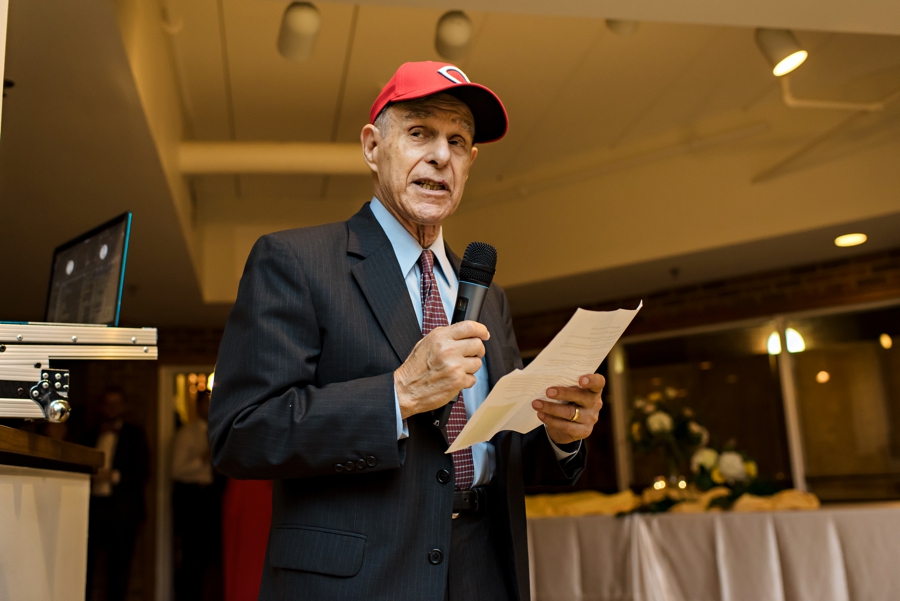 The brides grandfather giving a speech at the reception wearing a Cubs baseball hat.